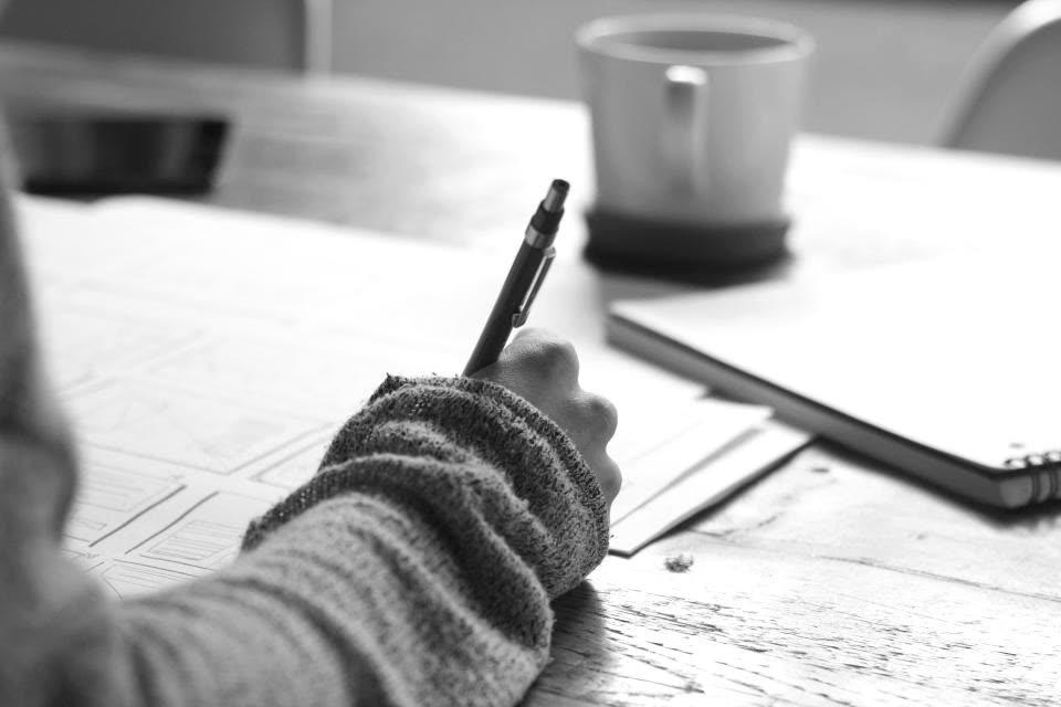 A hand marking up printed sheets on a table in soft window light.